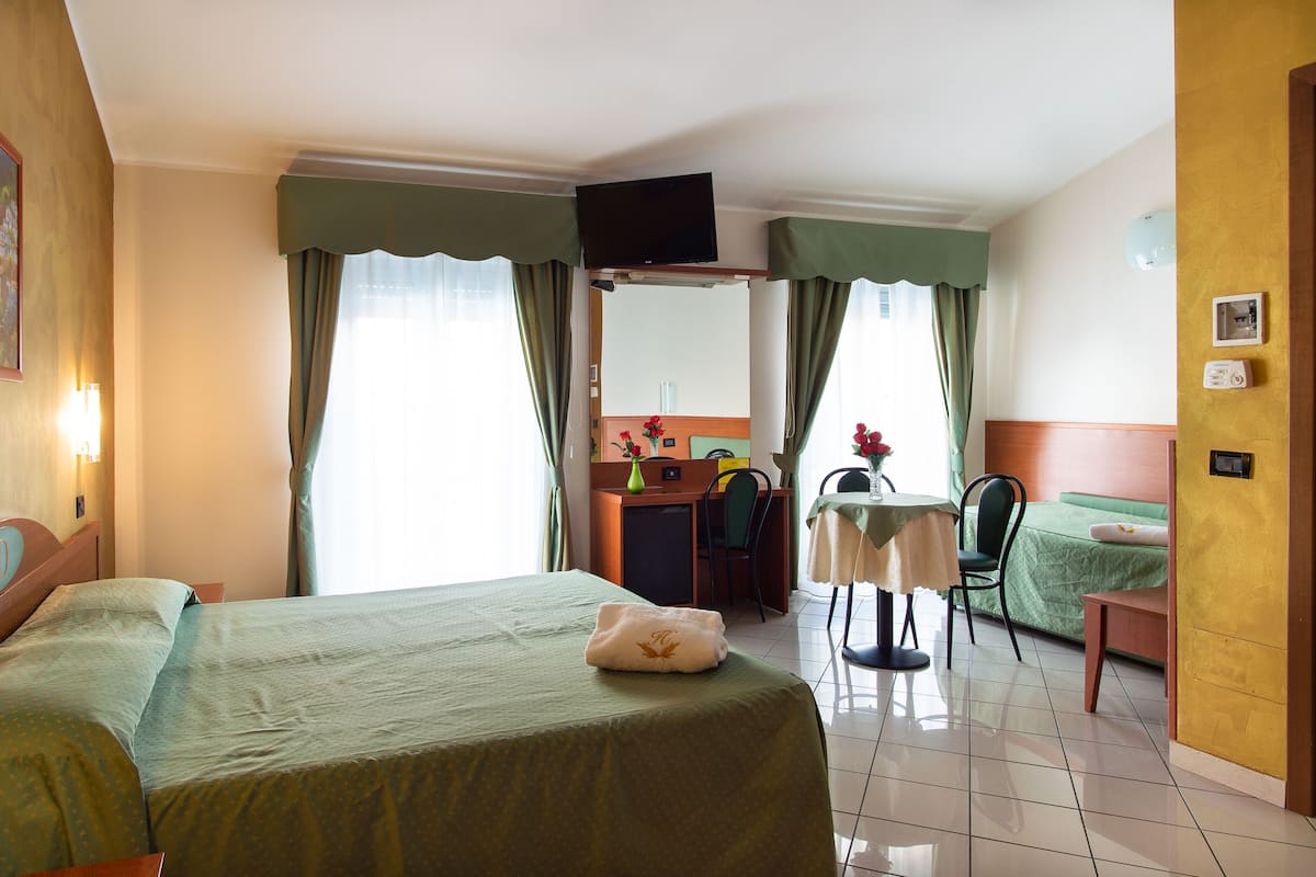 A hotel room with a bed, a desk, a chair, a small table, and a TV.