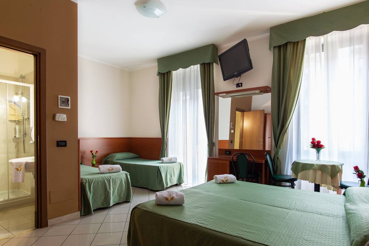 A hotel room with two beds, a TV, a desk, and a bathroom with a shower.