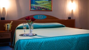 A hotel room with a bed, a bedside table with a champagne bottle, two glasses, and a vase with roses. There is a painting on the wall and a sign with the letters "HD". - HD Hotel (Milan)