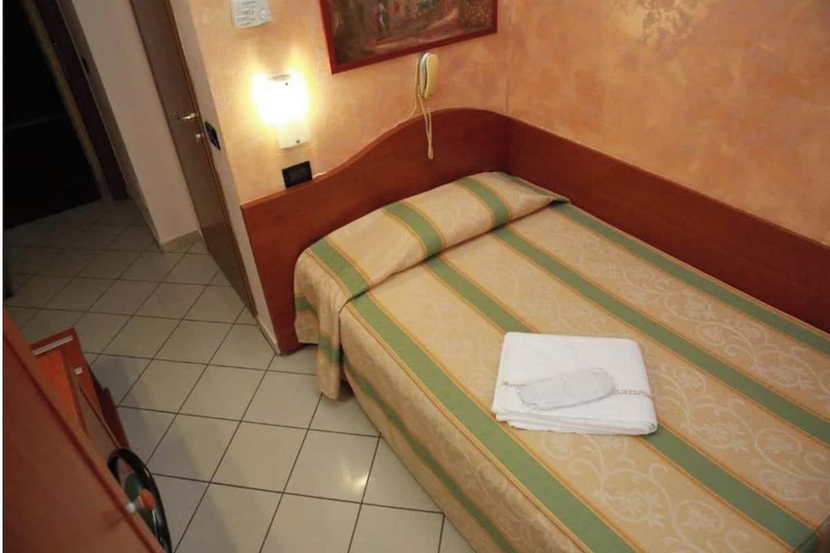 A hotel room with a single bed, a bedside telephone, and a wall-mounted light.