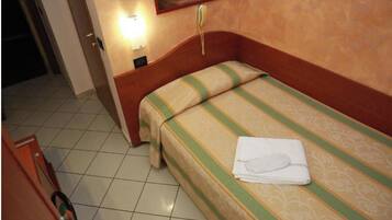 A hotel room with a single bed, a bedside telephone, and a wall-mounted light.