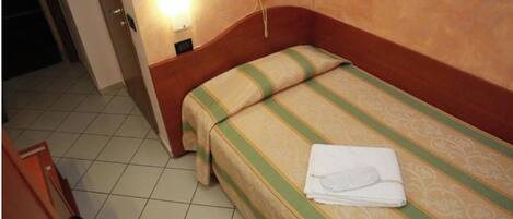 Une chambre d’hôtel avec un lit simple, un téléphone sur la table de chevet et une lampe fixée au mur.