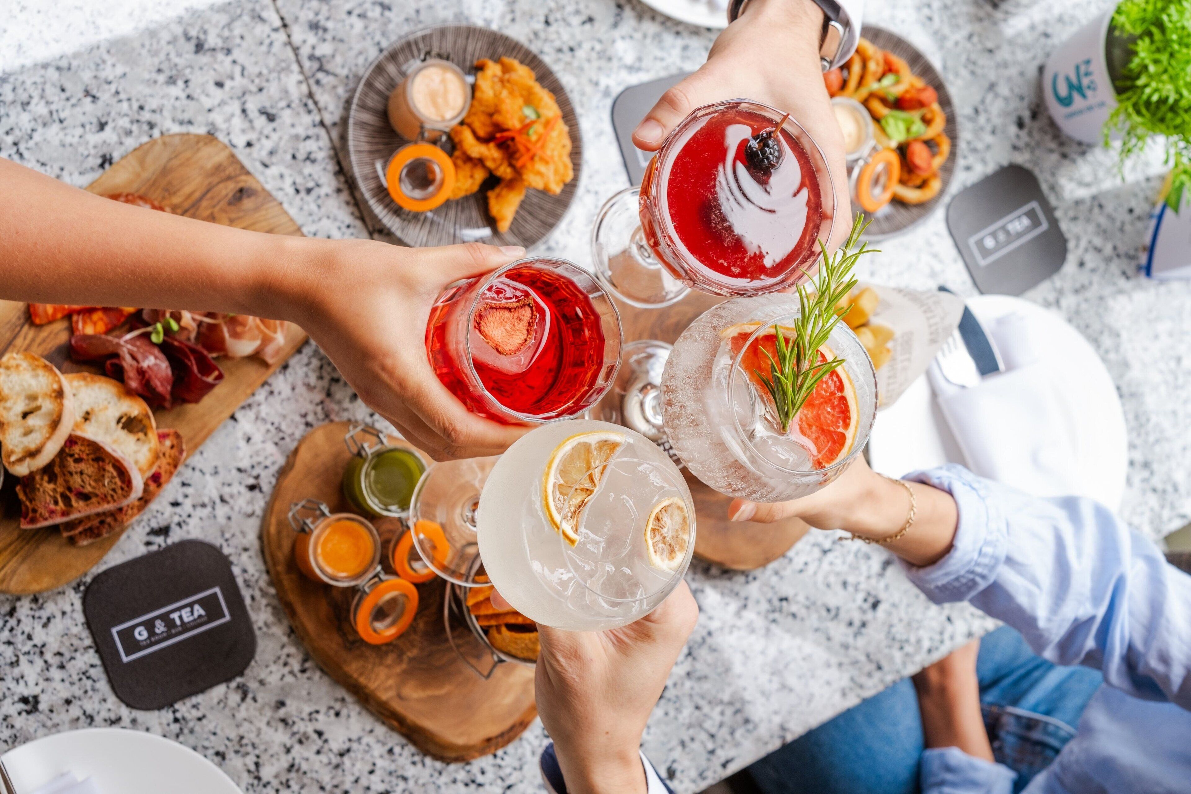A group of people holding drinks at a table with various food items and condiments.