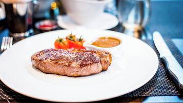 A plate with a grilled steak, a small bowl of sauce, and a garnish of tomatoes and herbs.