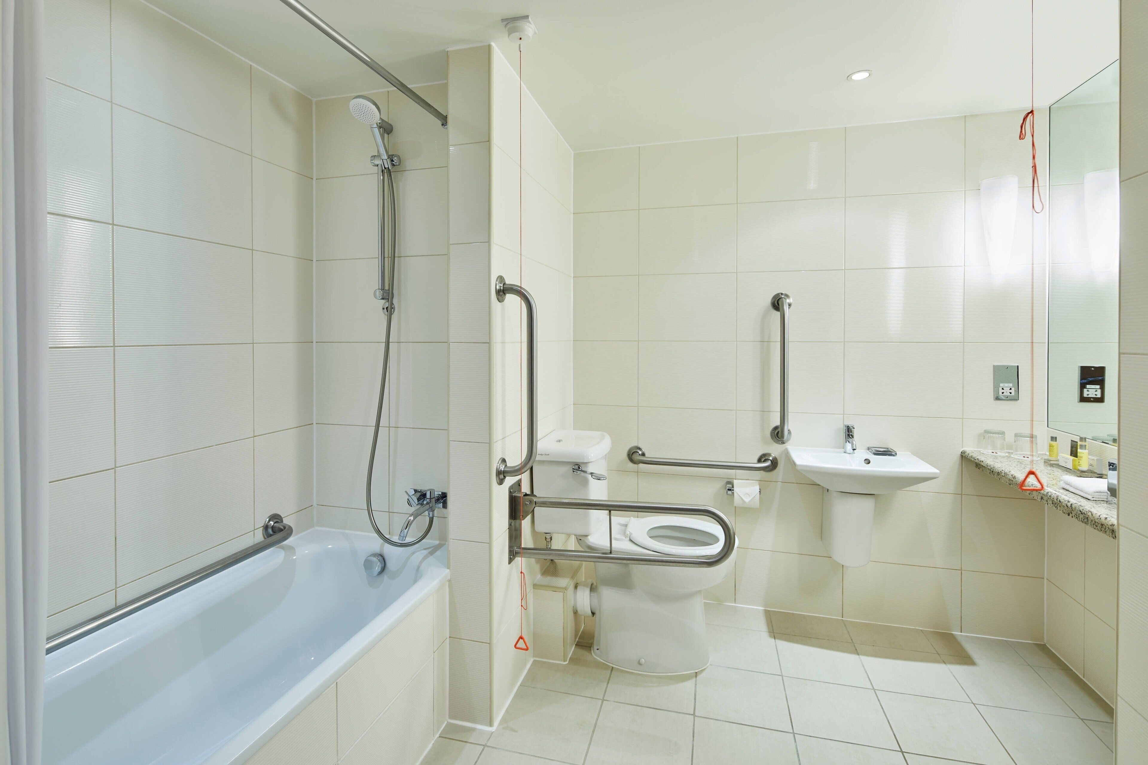 Een moderne badkamer met een badkuip, toilet en wastafel, voorzien van handgrepen en een douche.