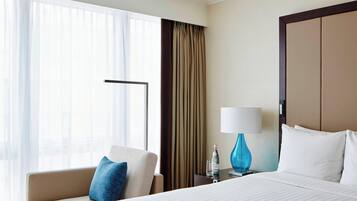 Een hotelkamer met een bed, een stoel, een nachtkastje met een lamp en een raam met gordijnen.