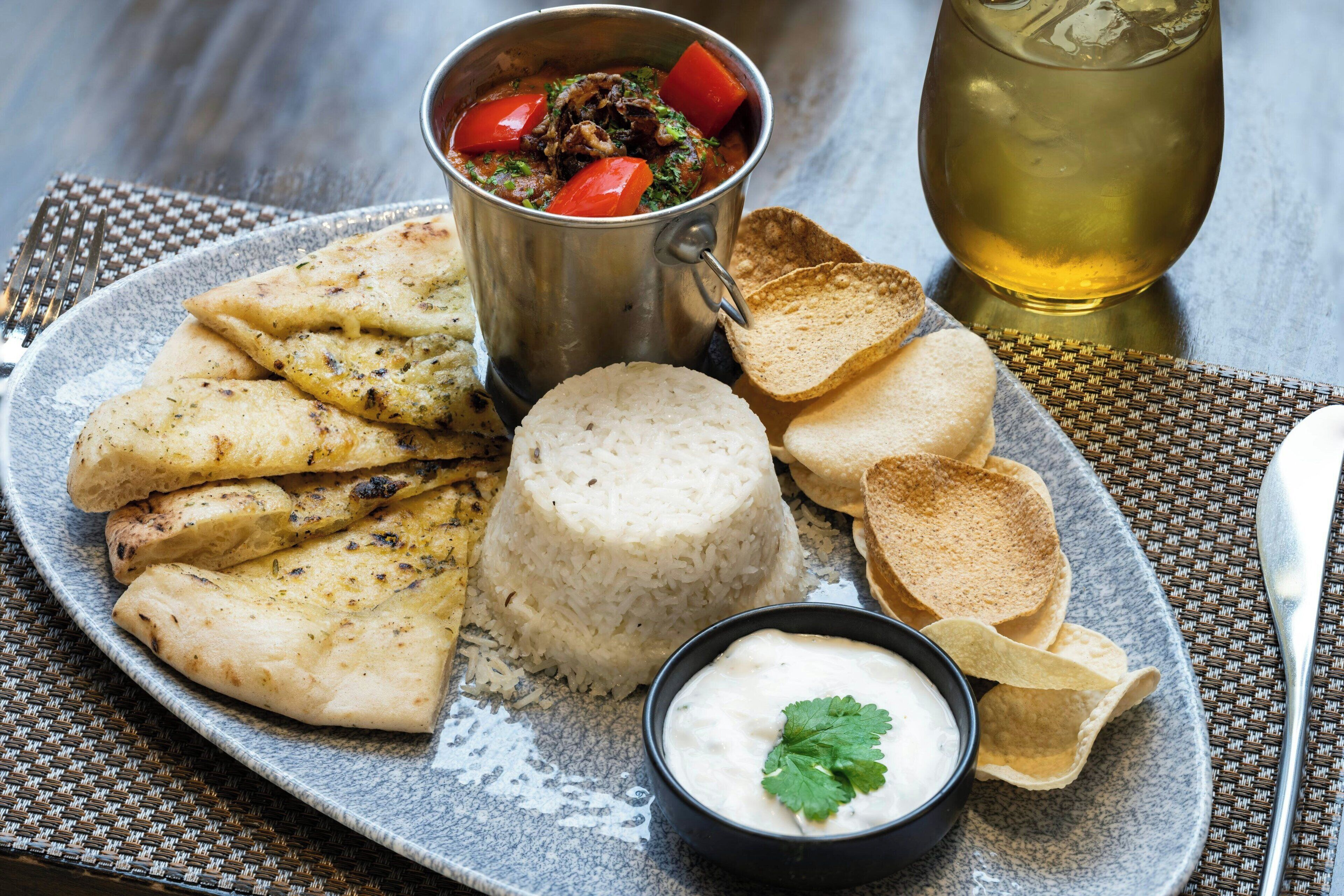 A plate with grilled chicken, rice, flatbread, and a bowl of sauce, accompanied by a drink and a glass.