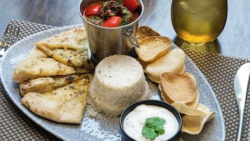 A plate with grilled chicken, rice, flatbread, and a bowl of sauce, accompanied by a drink and a glass.
