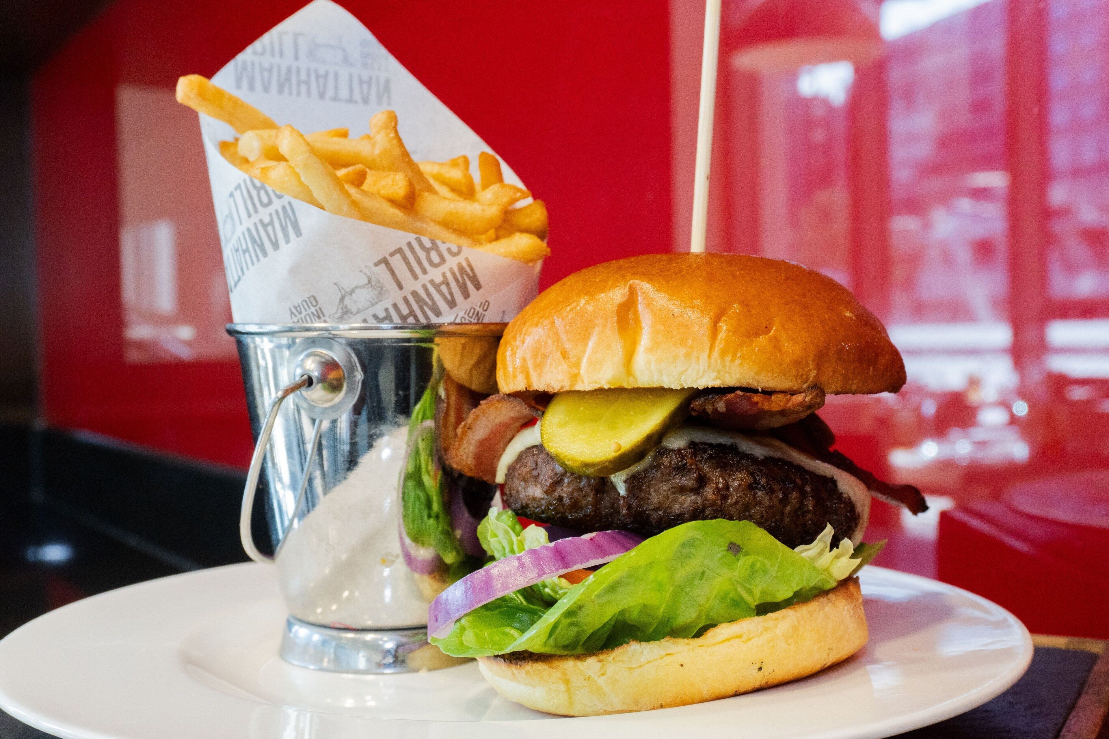 A burger with fries on a white plate, placed on a table with a red background.