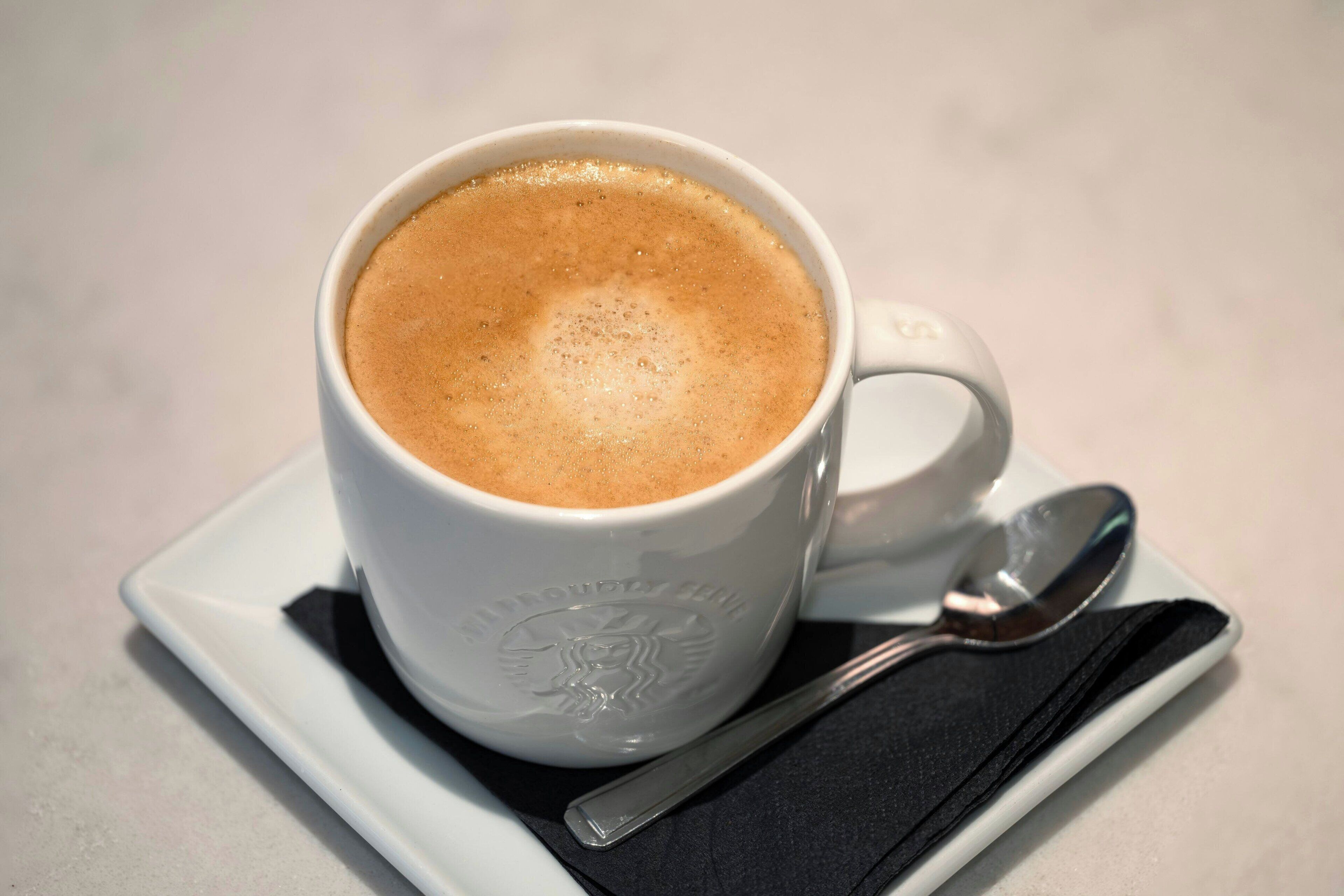 A white Starbucks cup with a spoon on a black napkin, placed on a white plate.