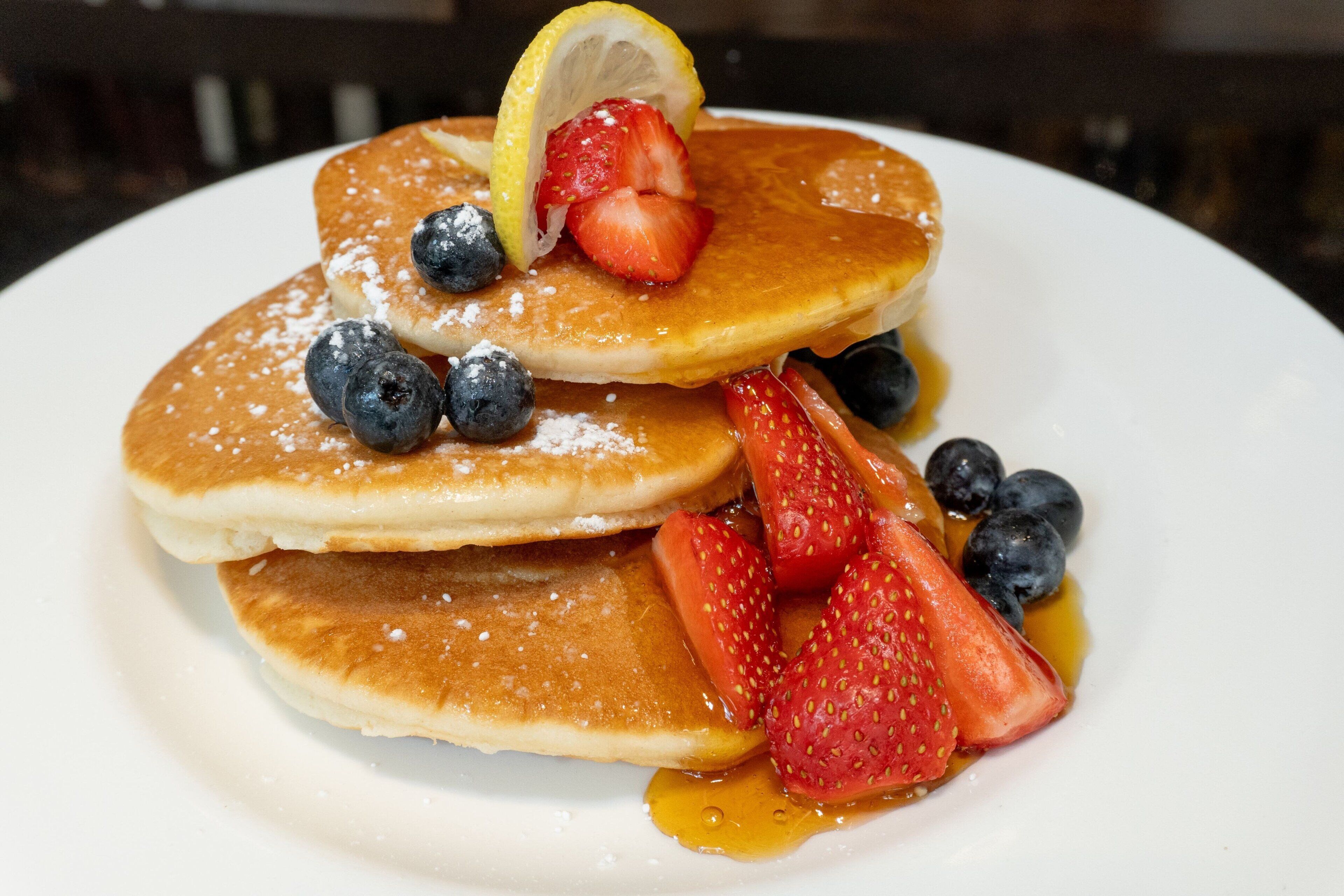 A stack of pancakes with strawberries and blueberries on a white plate.
