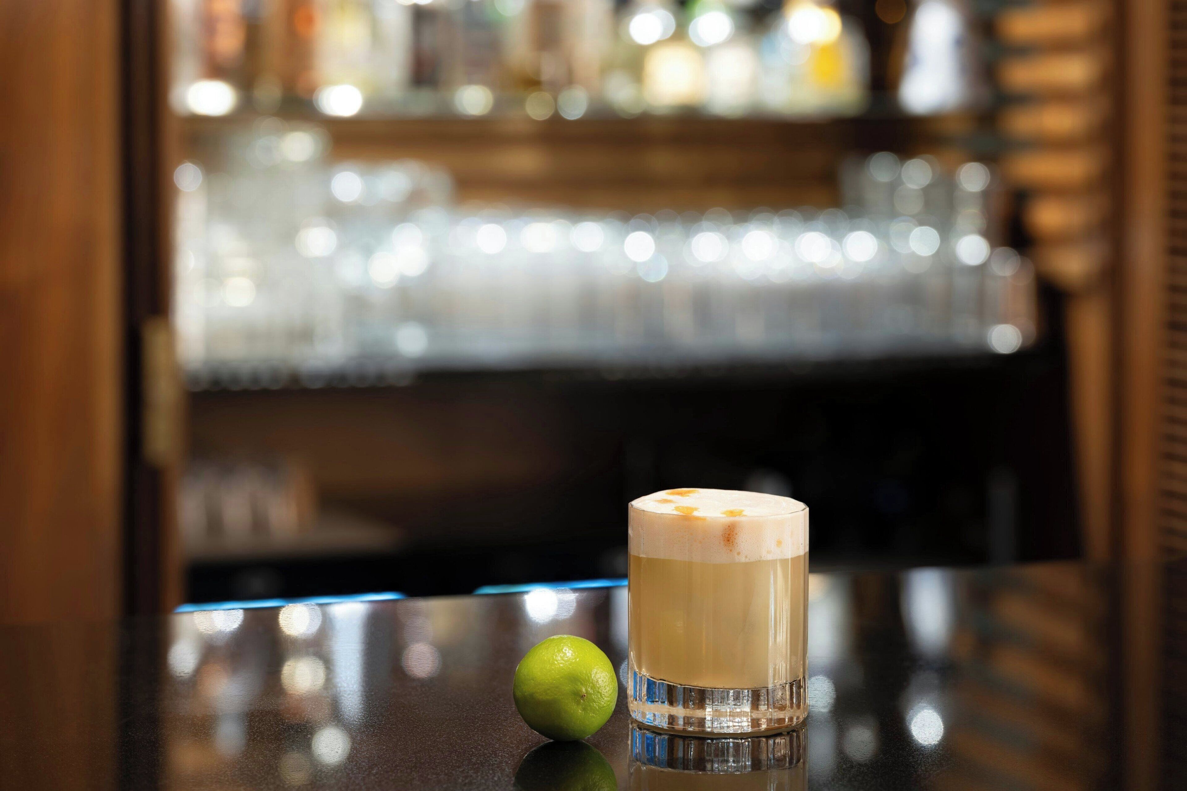 A bar setting with a glass of a layered beverage and a lime on a reflective surface.