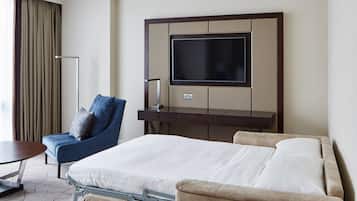 Een hotelkamer met een bed, een stoel, een bureau en een aan de muur bevestigde televisie.