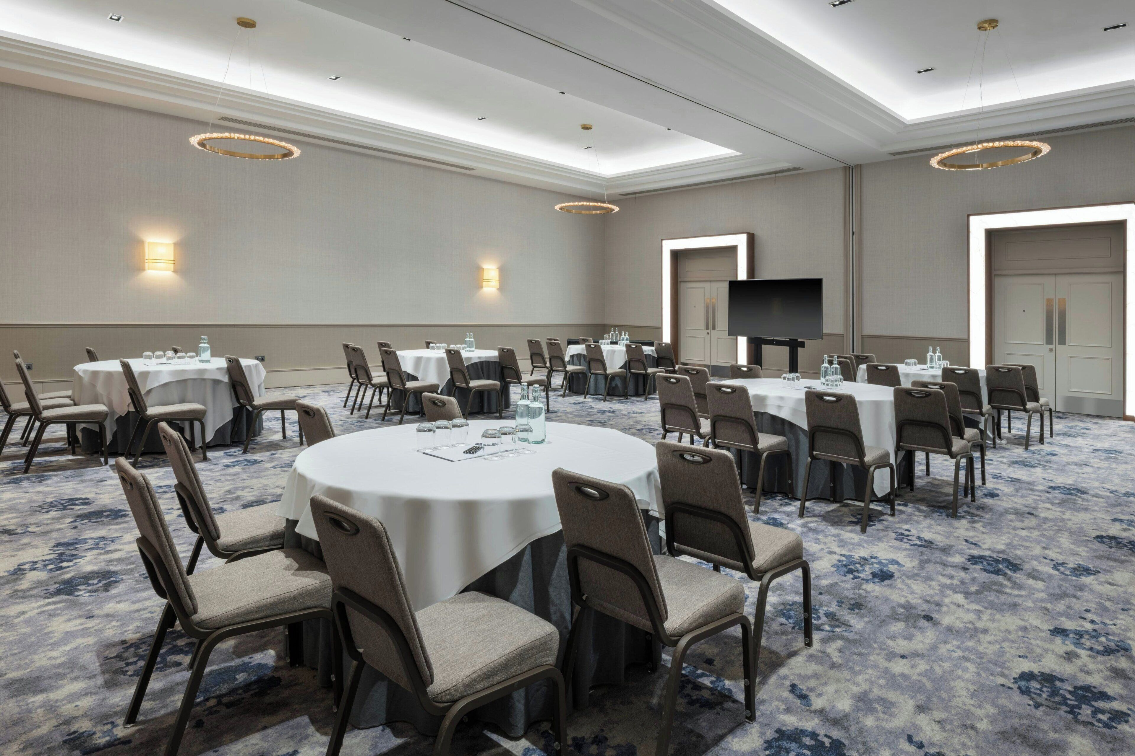 A conference room with round tables and chairs, a flat-screen TV, and a carpeted floor.