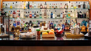 Een bar met diverse drankflessen op planken en een assortiment fruit en snacks op de toonbank.