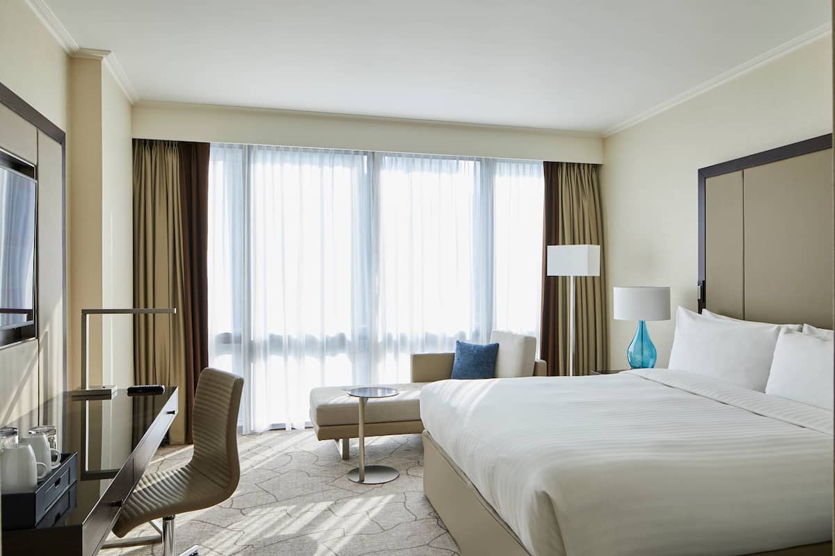 Ein Hotelzimmer mit einem großen Bett, einem Schreibtisch mit Stuhl, einem kleinen Tisch und einem Fernseher.