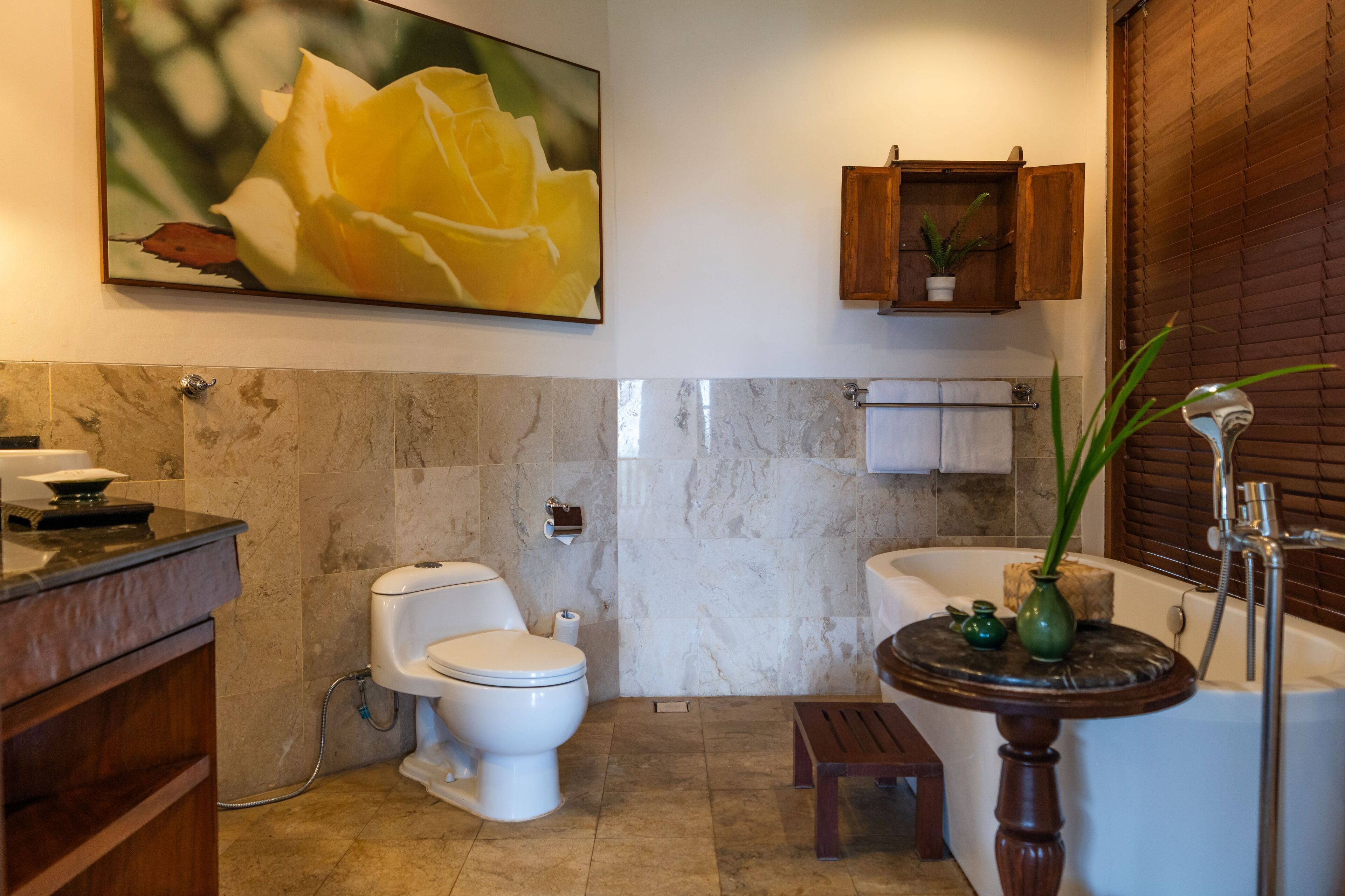A bathroom with a toilet, sink, and bathtub. There is a wooden cabinet above the sink and a painting of a flower on the wall.