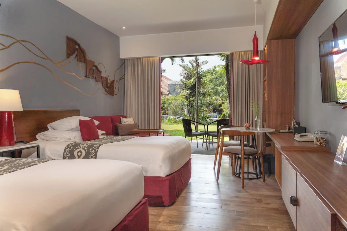 A hotel room with two beds, a dining area, and a view of the garden.