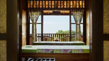 Relax on the balcony overlooking a lush landscape, featuring a table and a comfortable bed with a floral-patterned bedspread.