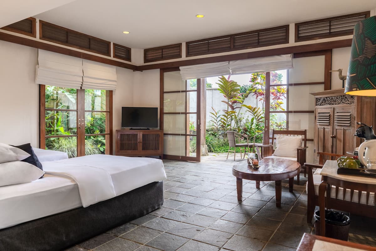 A hotel room with a bed, a TV, a dining table, and a view of the garden.