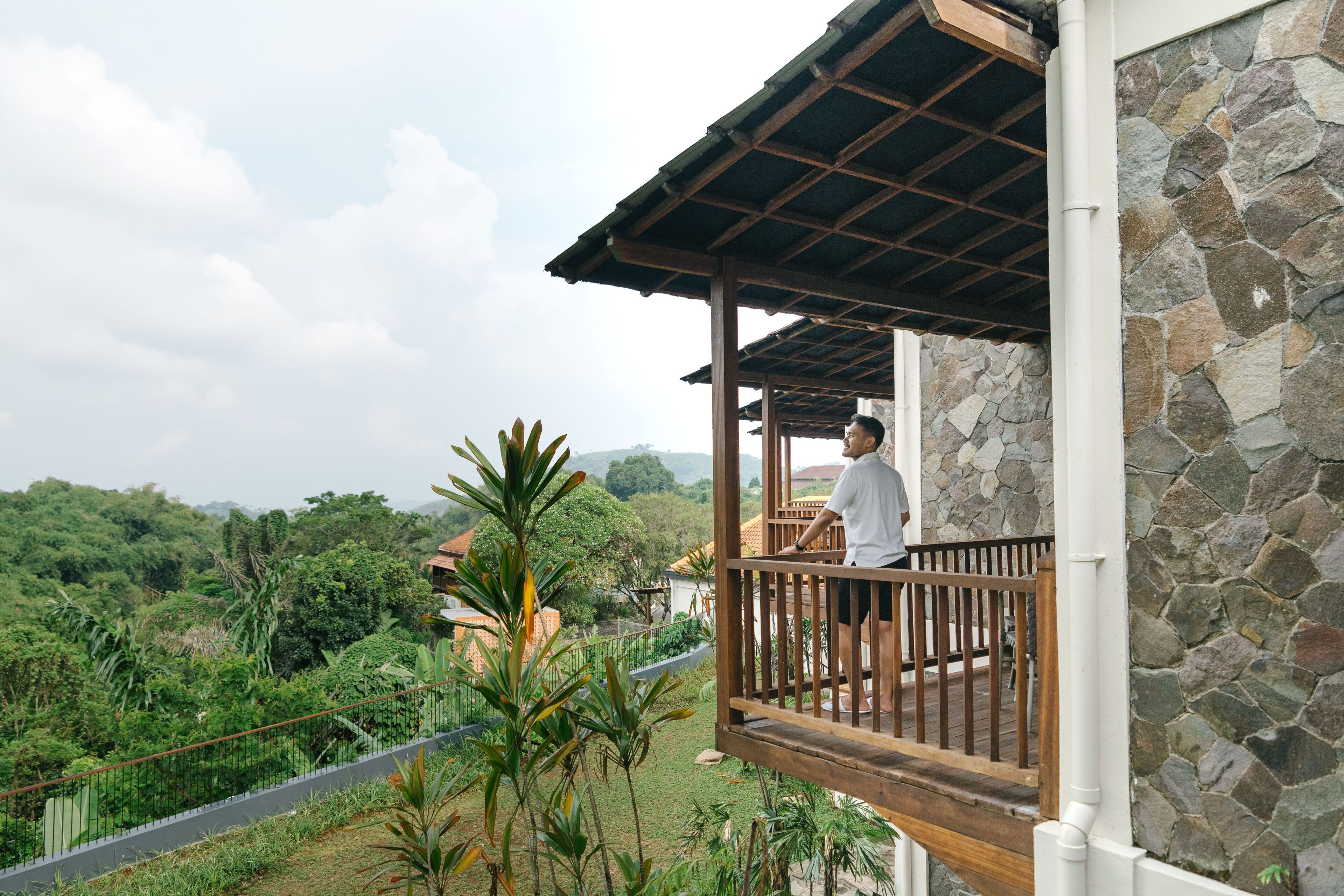A balcony with a stone wall and wooden railing overlooking a lush landscape.