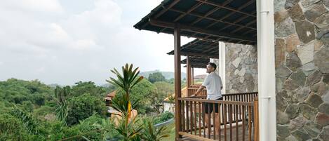 A balcony with a stone wall and wooden railing overlooking a lush landscape.