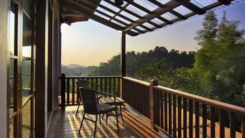 Una terraza de madera con una silla, puertas de cristal y vistas a árboles y montañas.