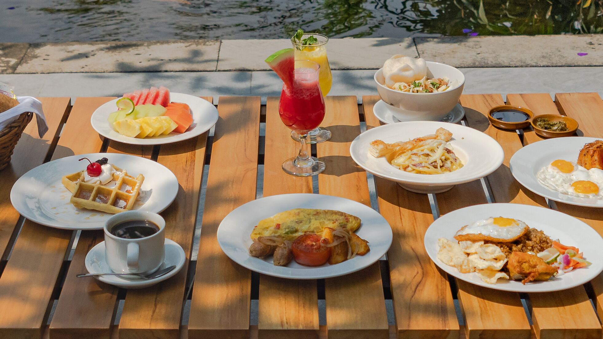 Una mesa de madera con diversos platos de desayuno, como waffles, huevos y una ensalada de frutas.