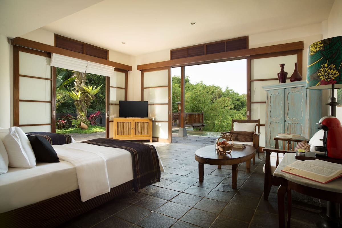 A spacious bedroom with a large bed, a television, a wooden cabinet, and a view of the garden through large sliding doors.