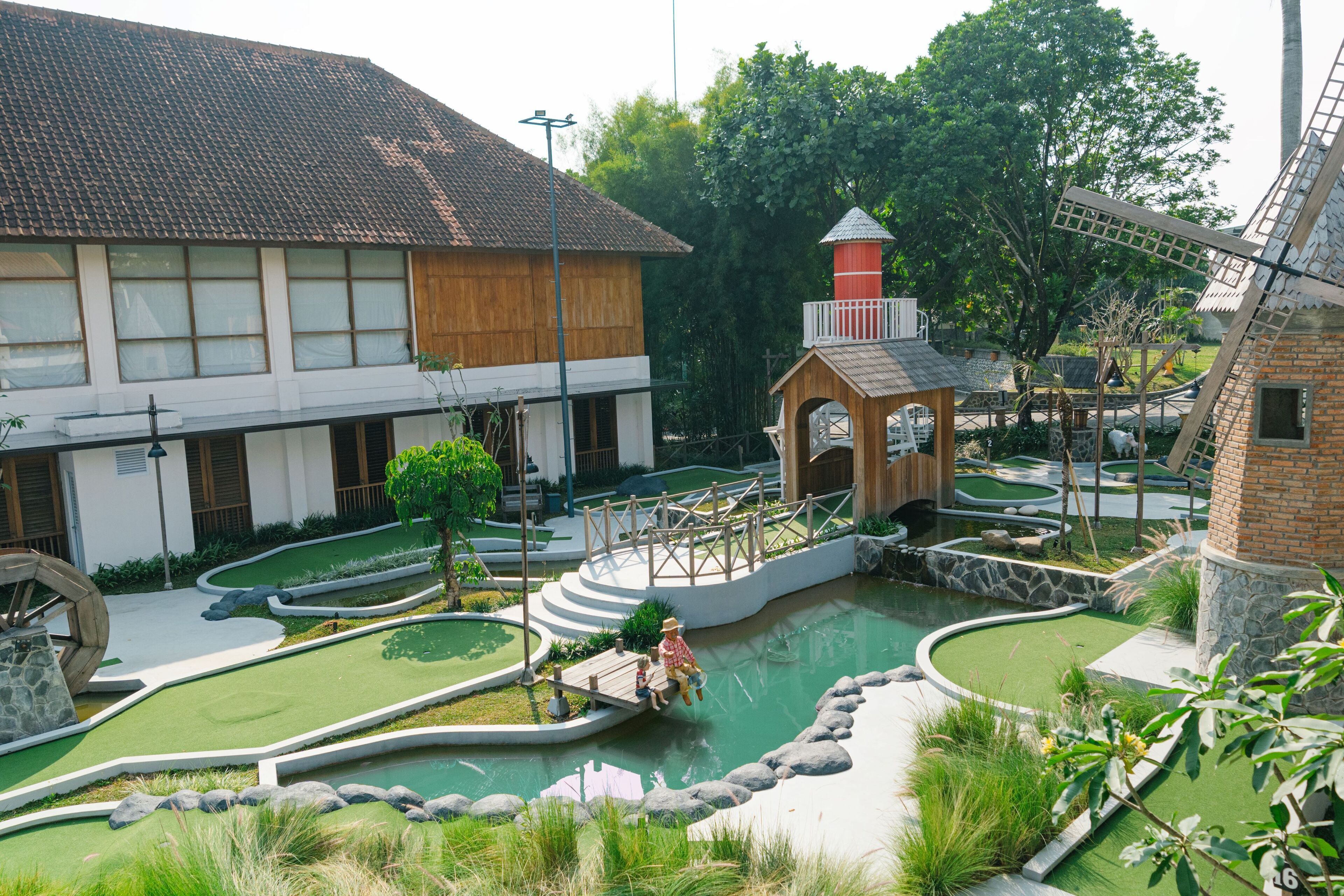 A miniature golf course with a windmill, a wooden structure, and a pond.