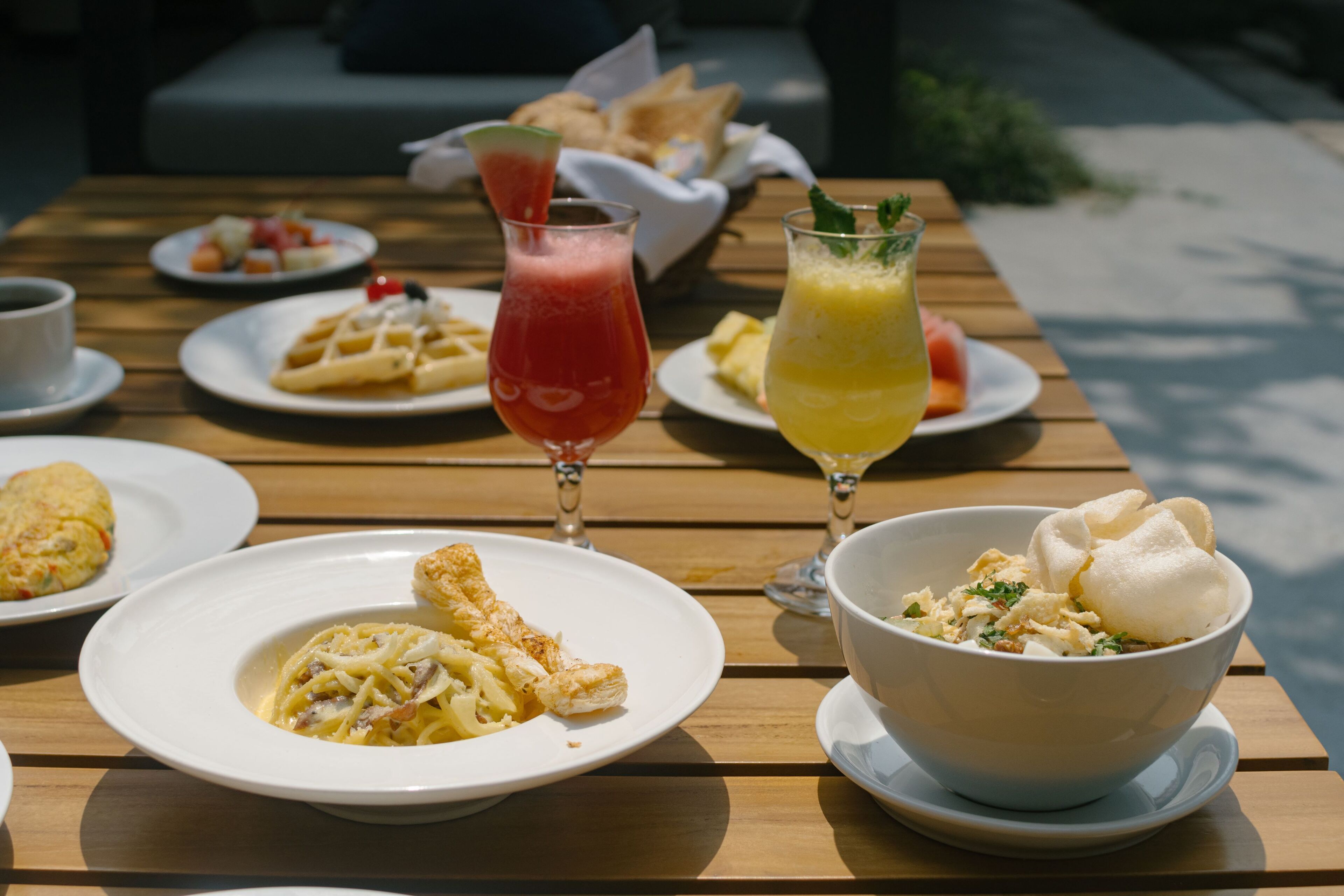 A wooden table with various dishes including pasta, waffles, and a bowl of soup.