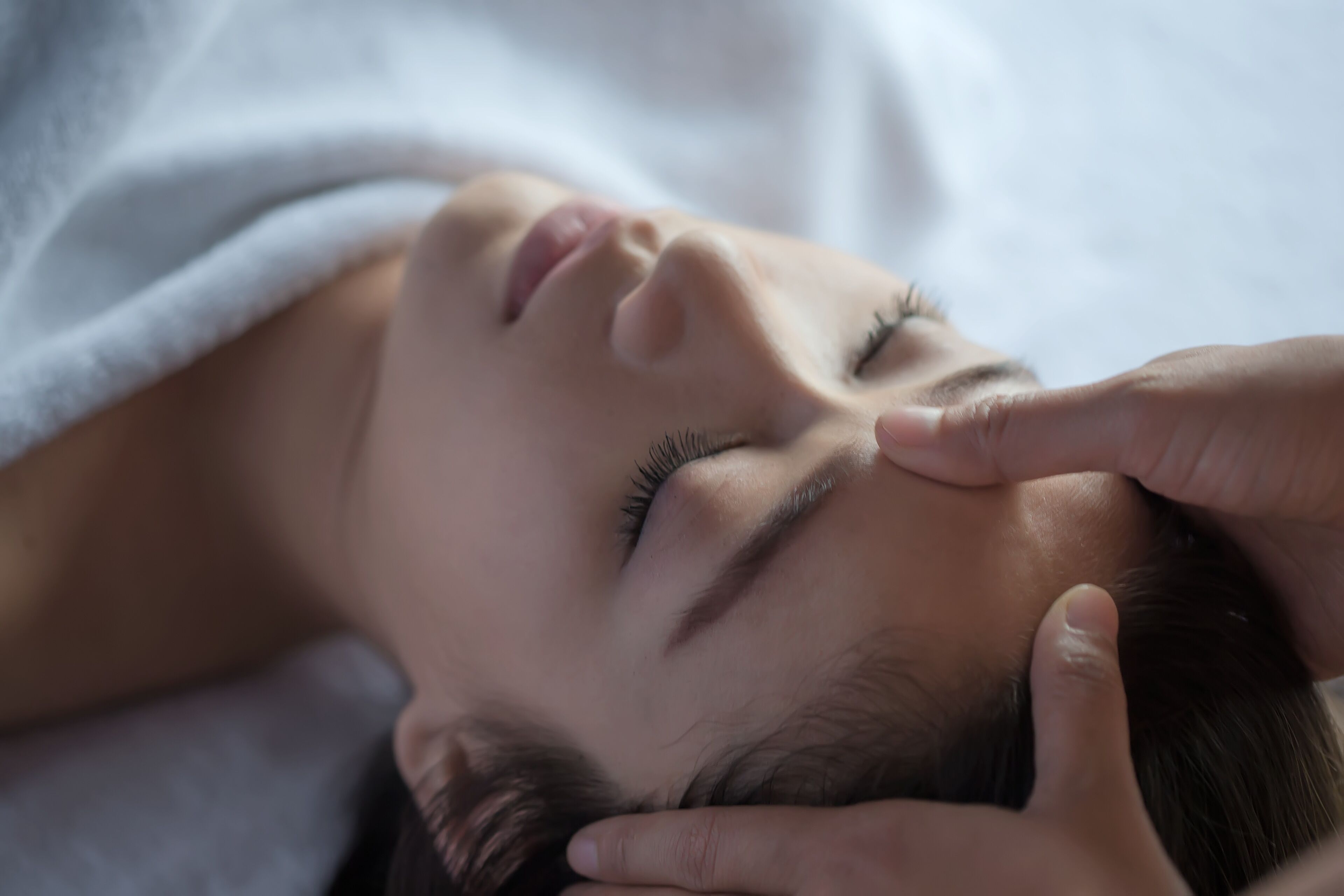A person lying down with a hand on their forehead, possibly in a relaxed or resting position.