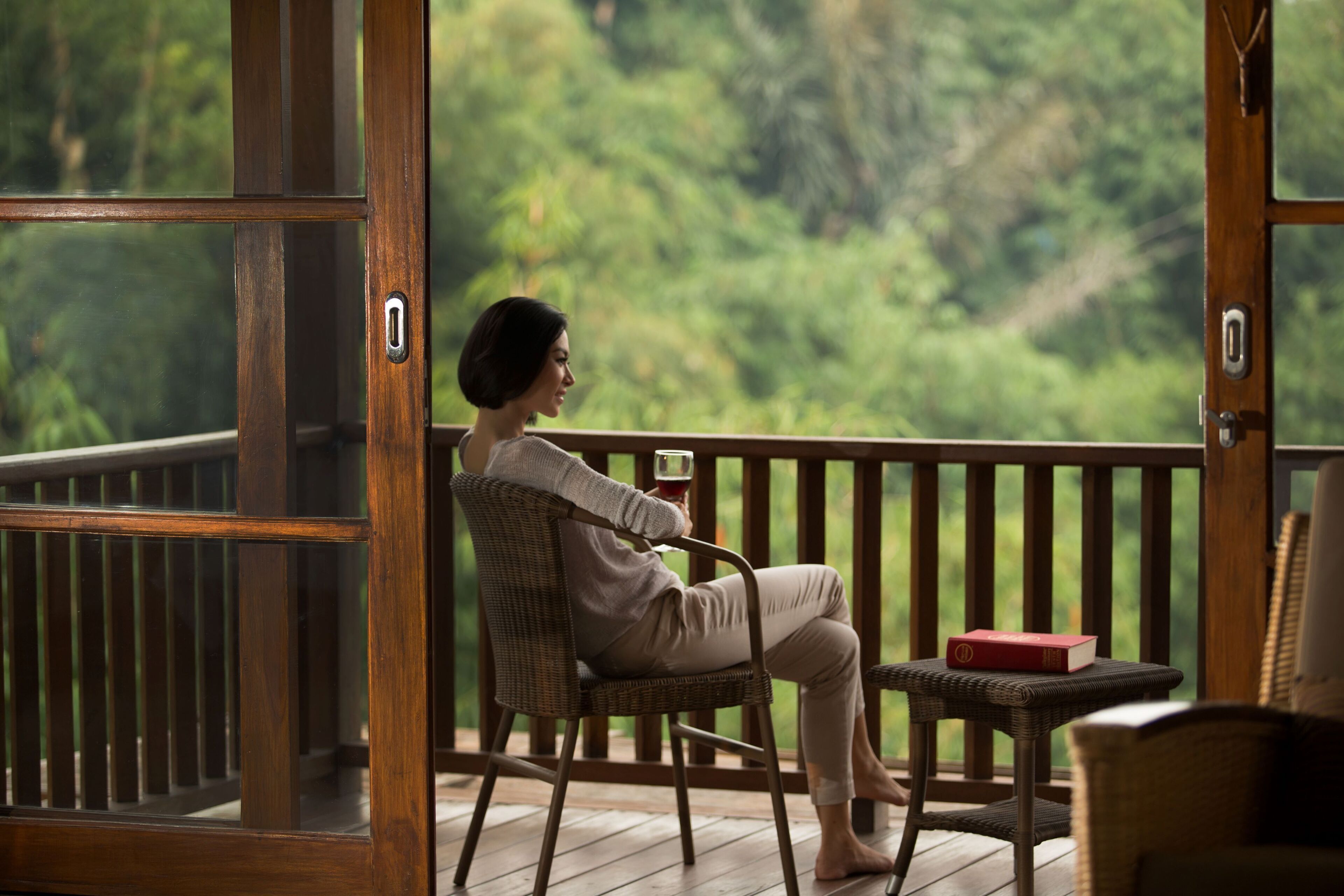 A person sitting on a wicker chair on a wooden deck with a view of a forest.