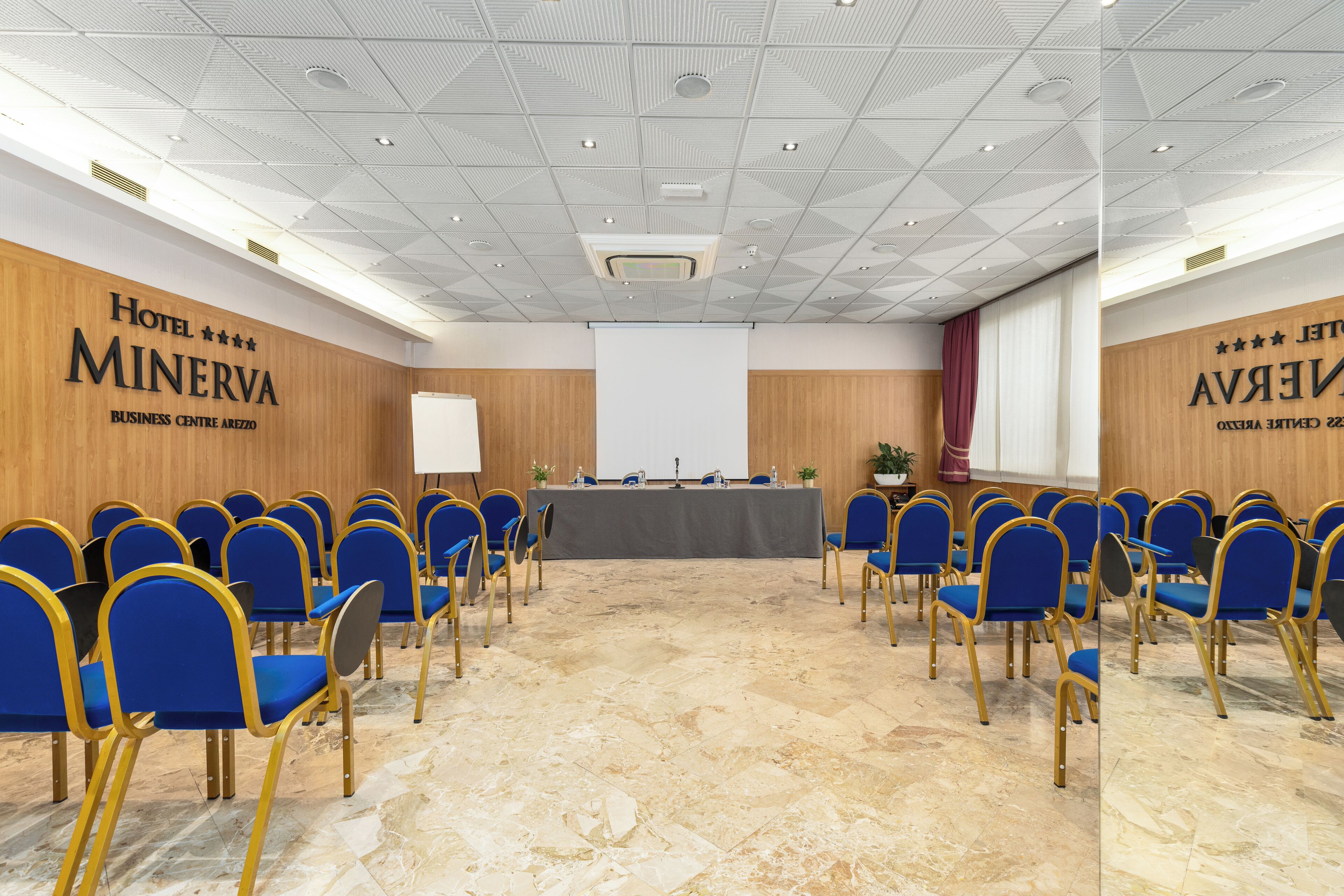 A conference room with blue chairs, a long table, and a projector screen.