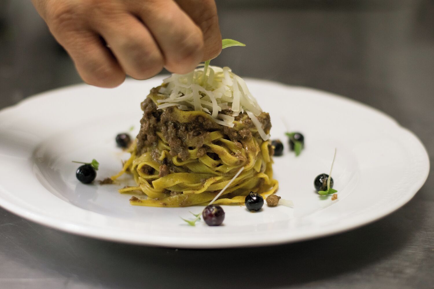 A plate of pasta with a hand adding garnish.
