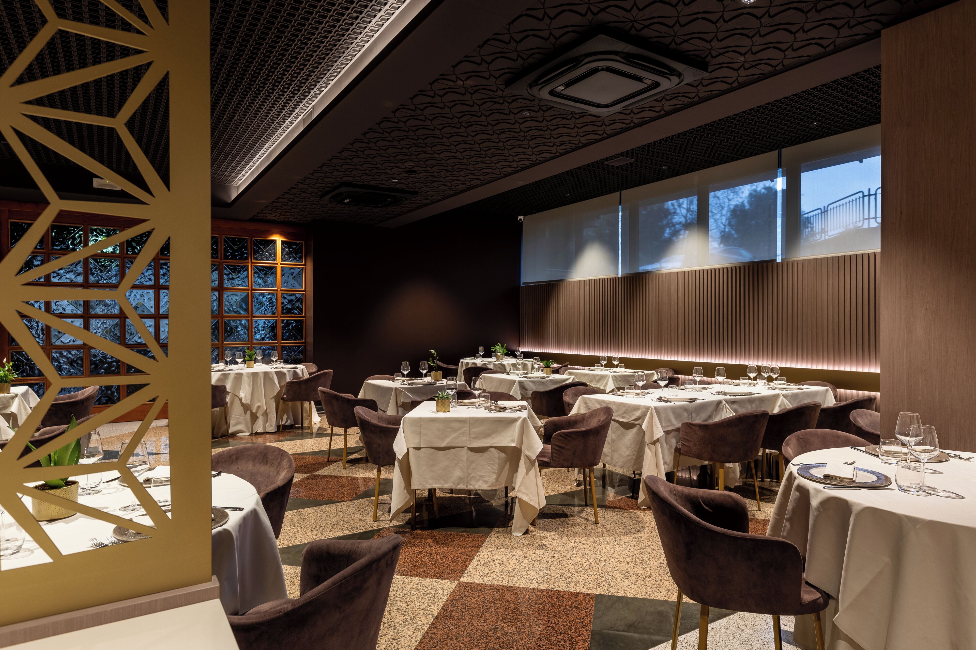 Un restaurante con varias mesas redondas, sillas y una gran pantalla de proyección en la pared.
