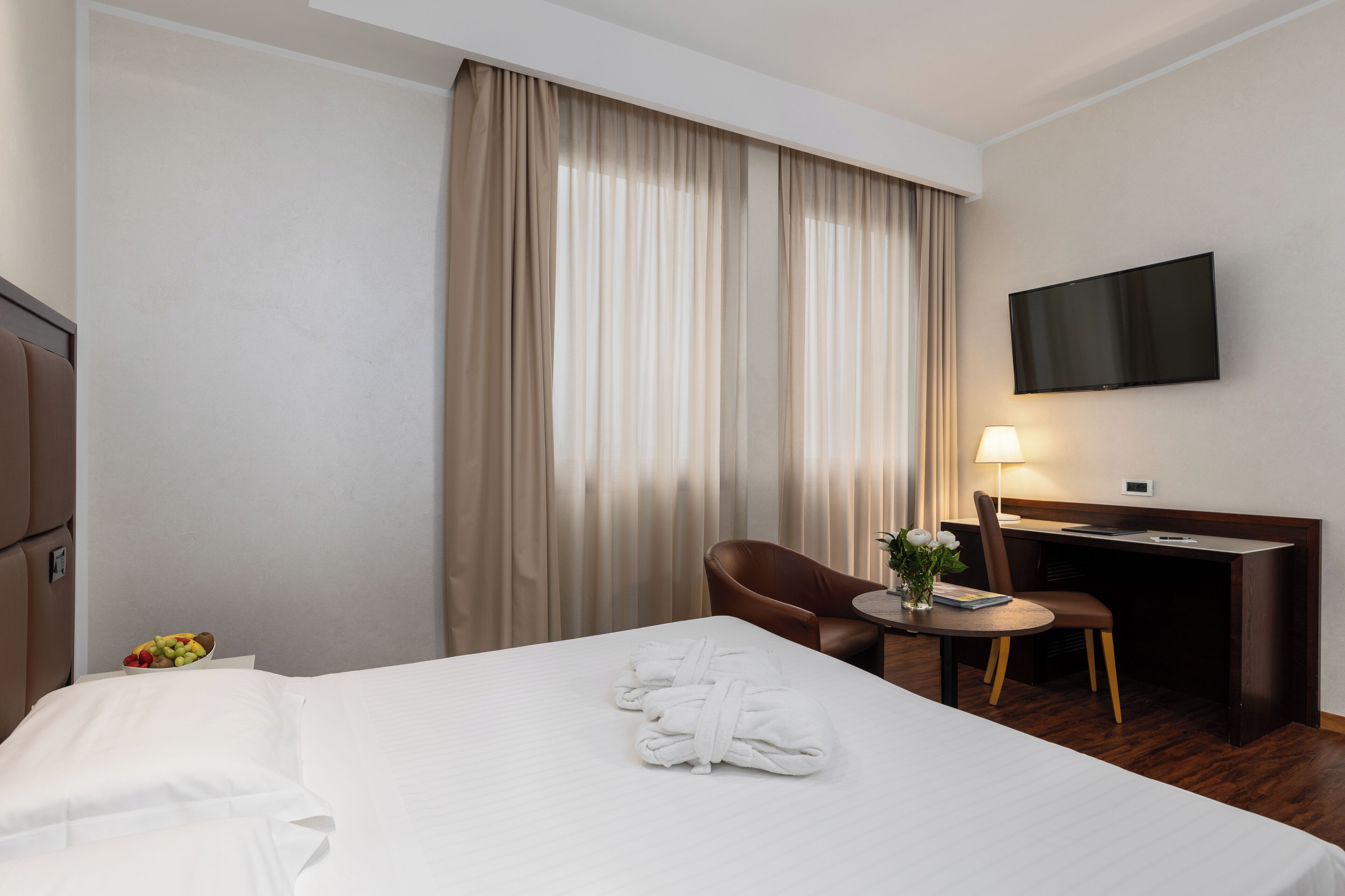 A hotel room with a bed, a desk, a chair, a TV, and a lamp.