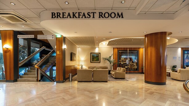 A spacious breakfast room with a modern design, featuring a wooden reception desk, comfortable seating, and a staircase leading to other areas. - Hotel Minerva (Arezzo)
