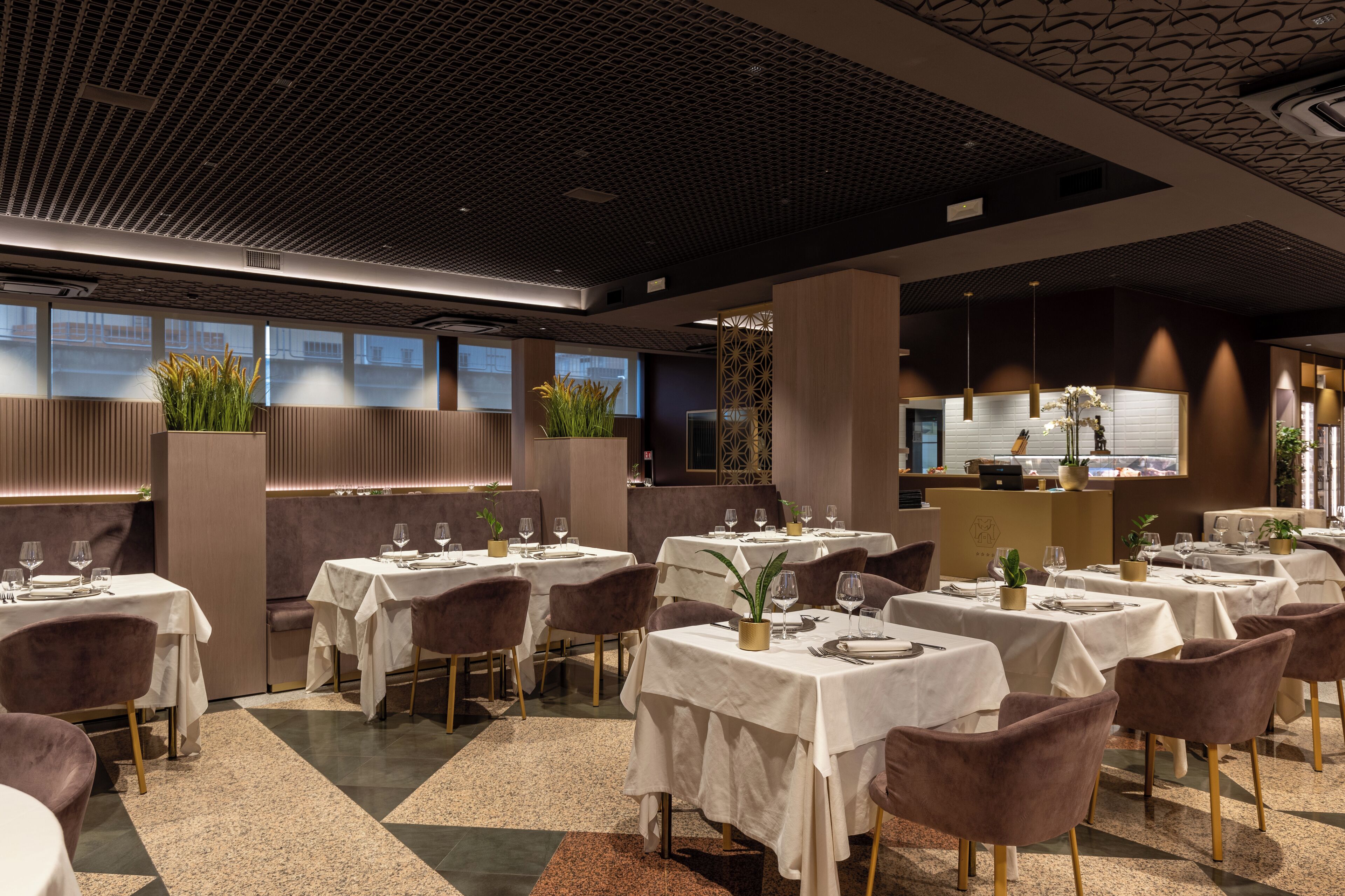 Un restaurante moderno con varias mesas y sillas, un techo con diseño y amplios ventanales.