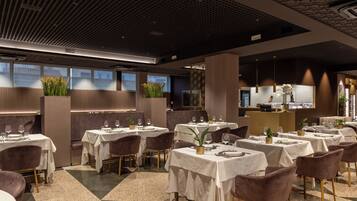 Un restaurante moderno con varias mesas y sillas, un techo con diseño y amplios ventanales.