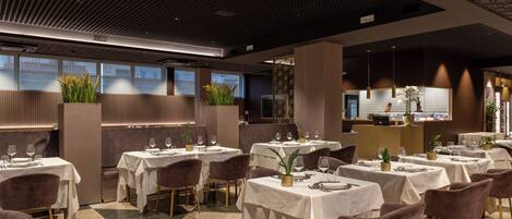 A modern restaurant with multiple tables and chairs, a patterned ceiling, and large windows.