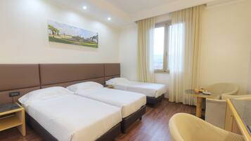 Habitación de hotel con dos camas, una mesita, una silla y un cuadro en la pared.