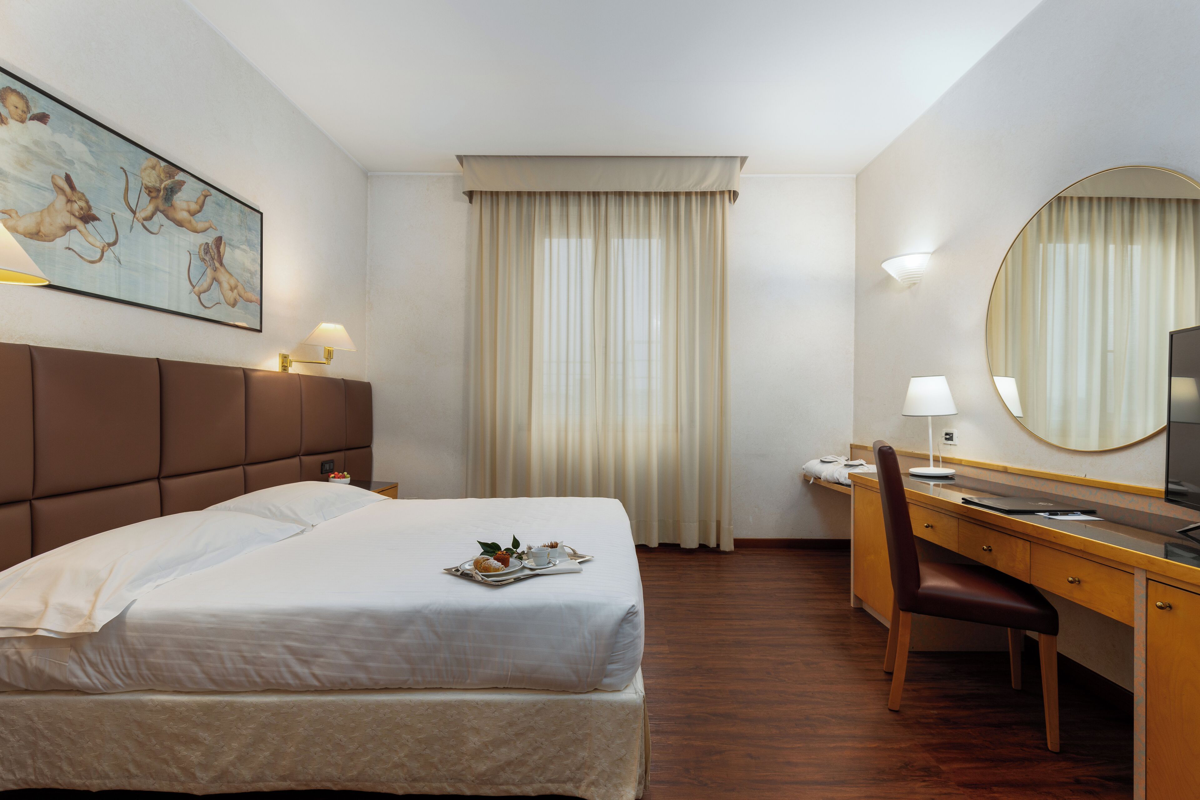 A hotel room with a bed, a desk, a chair, a television, and a painting on the wall.