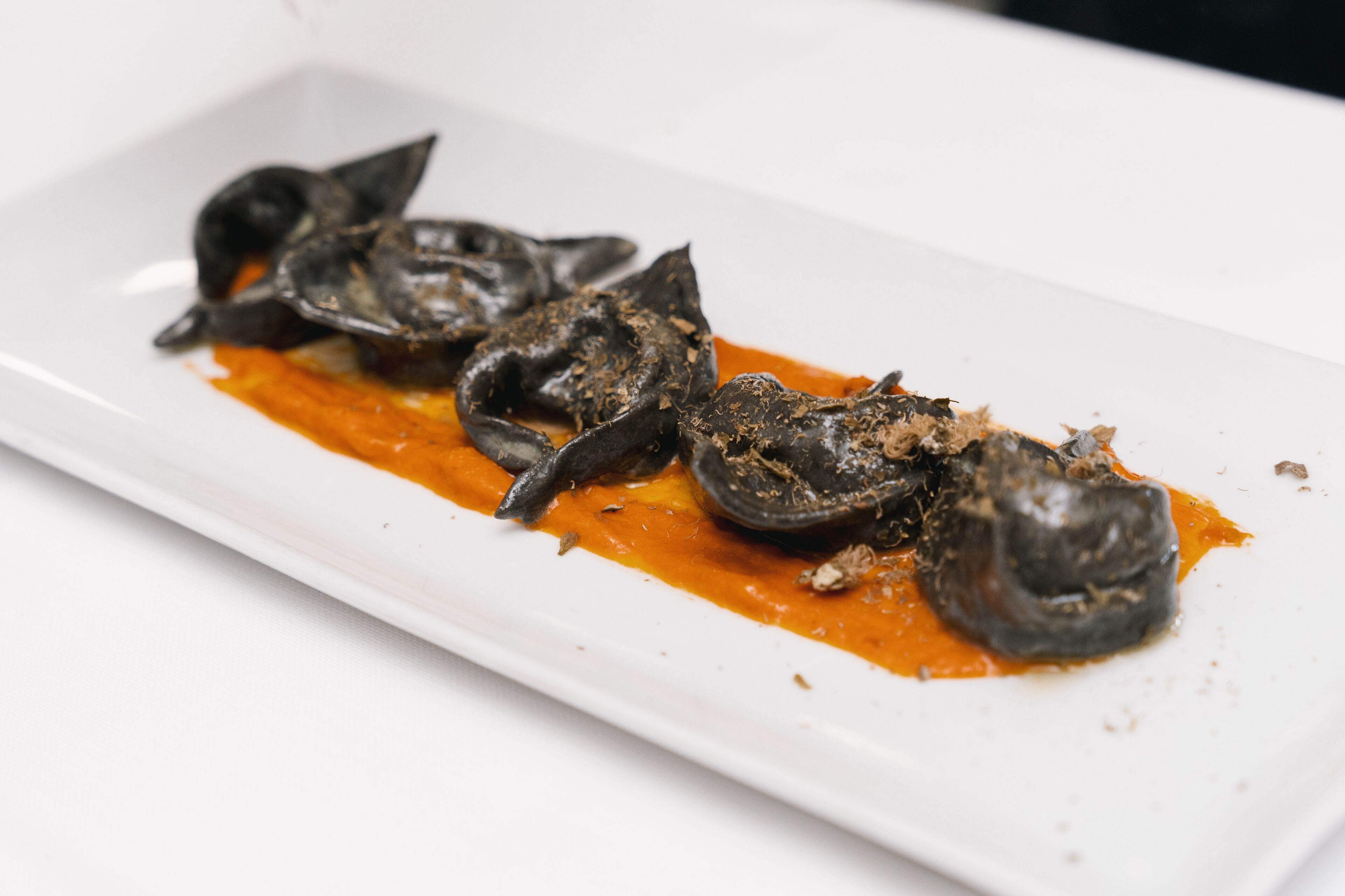 Un plato rectangular blanco con salsa oscura y un plato que parece ser de mariscos.