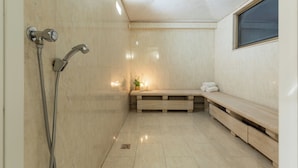 A modern bathroom with a bench, a shower with a handheld showerhead, and a window. - Hotel Minerva (Arezzo)