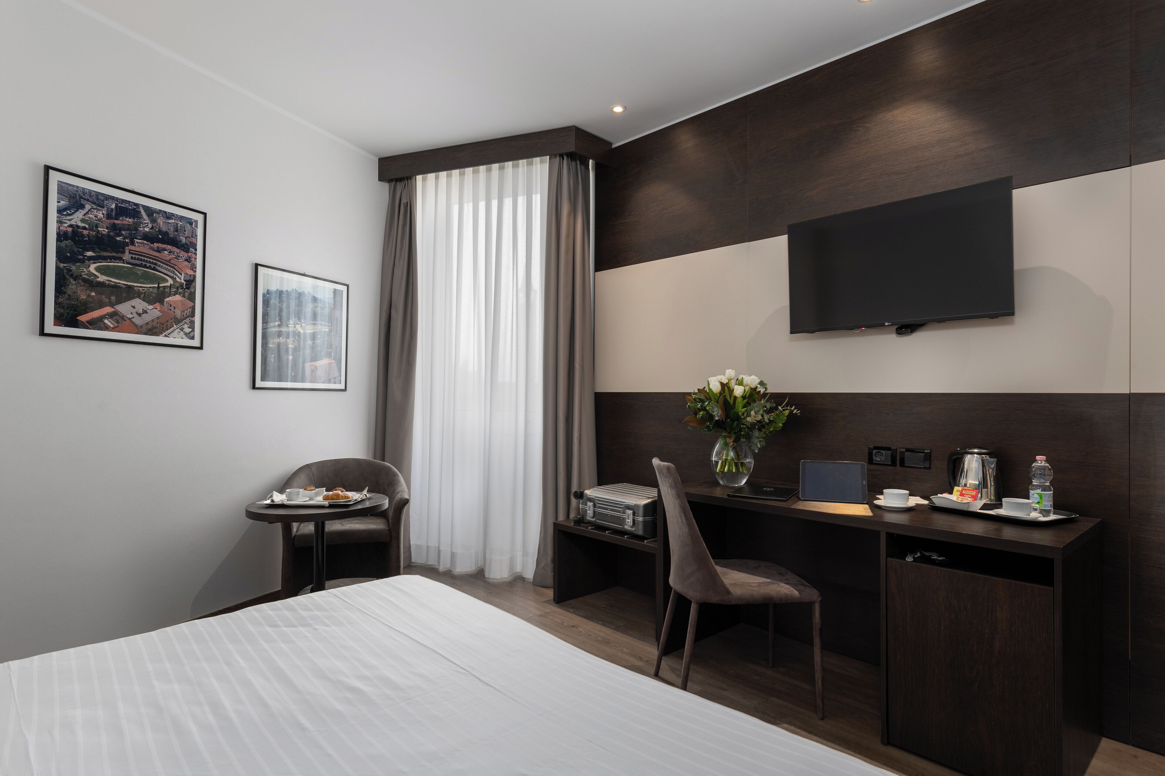 Habitación de hotel con cama, un escritorio con silla, un televisor montado en la pared y dos cuadros enmarcados.