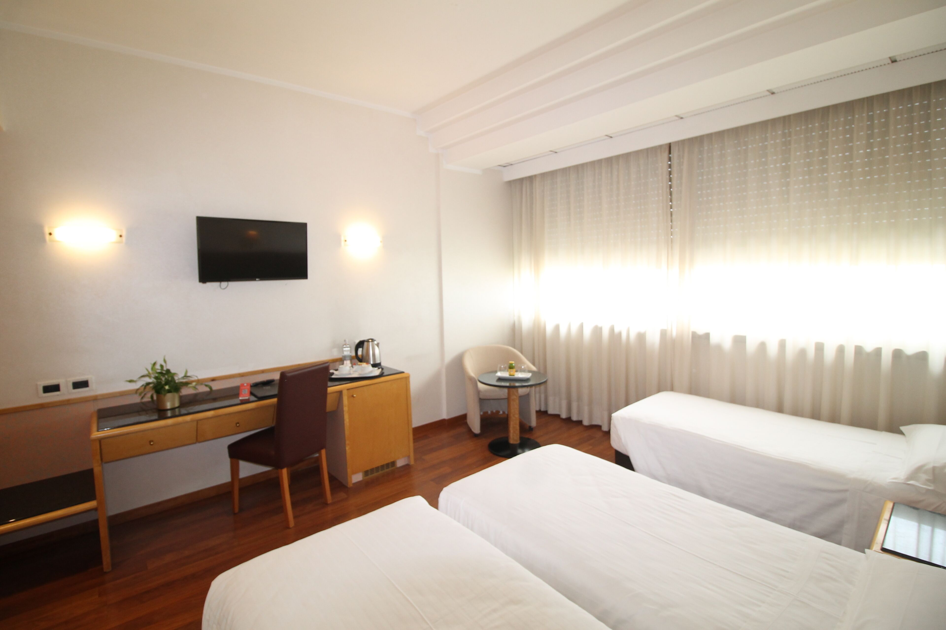 Una habitación de hotel con escritorio, dos camas, televisor y ventana con cortinas.