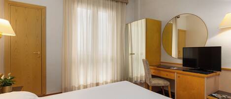 Une chambre d’hôtel comprenant un lit, un bureau avec une chaise, une télévision et un grand miroir.