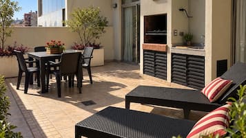 Une terrasse extérieure avec une table et des chaises pour les repas, un barbecue et des fauteuils de jardin.