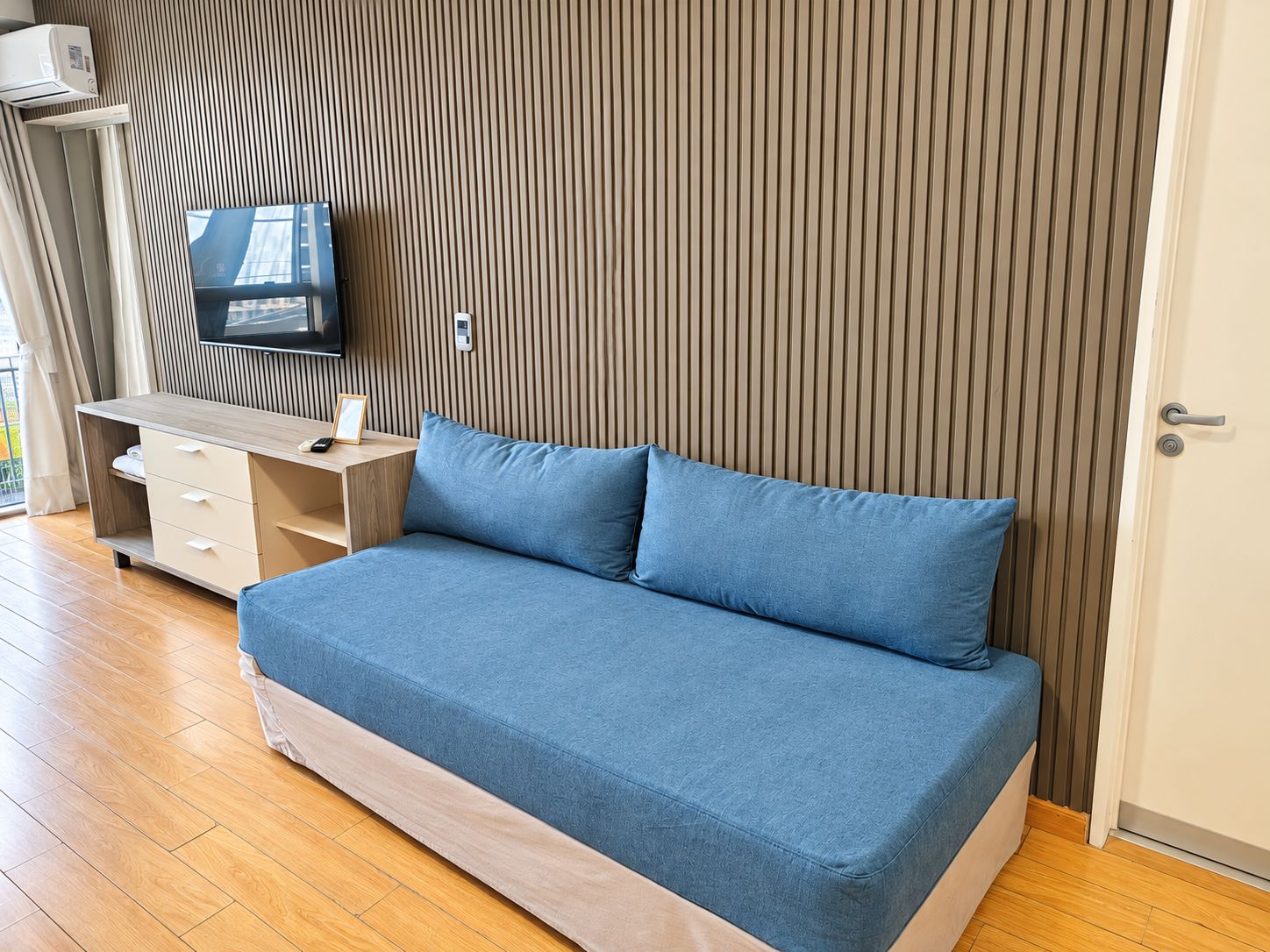 Une pièce comprenant un lit, un téléviseur fixé au mur, un mur recouvert de panneaux en bois et une porte.